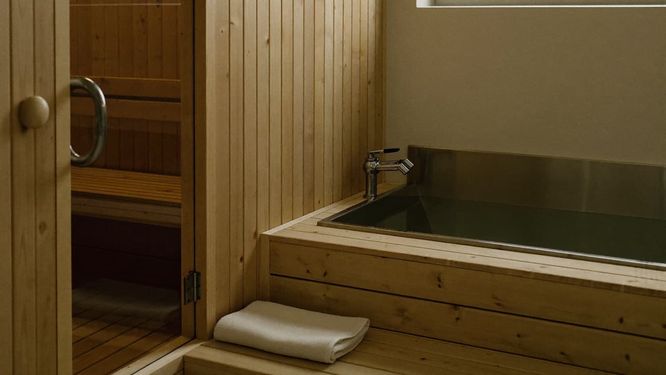A wooden sauna interior with soft light beside a cold immersion tub in a quiet wellness space