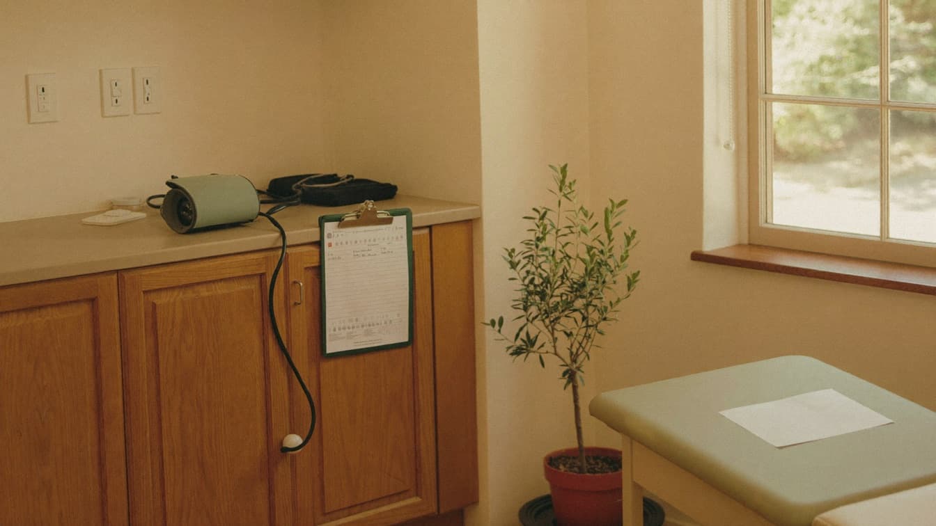 A calm primary care exam room with a blood pressure cuff and a clipboard on the counter.