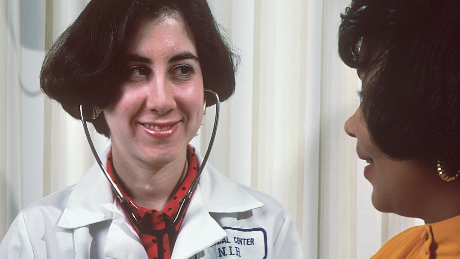 A primary care provider in a white coat talking with a patient during an annual wellness visit, modeling the kind of unhurried conversation a concierge physical allows.